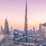 A modern international student with a laptop, smiling brightly on a vibrant campus with the iconic Dubai skyline in the background, representing the opportunity to study in Dubai.
