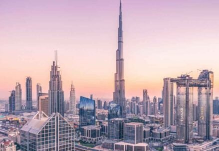 A modern international student with a laptop, smiling brightly on a vibrant campus with the iconic Dubai skyline in the background, representing the opportunity to study in Dubai.